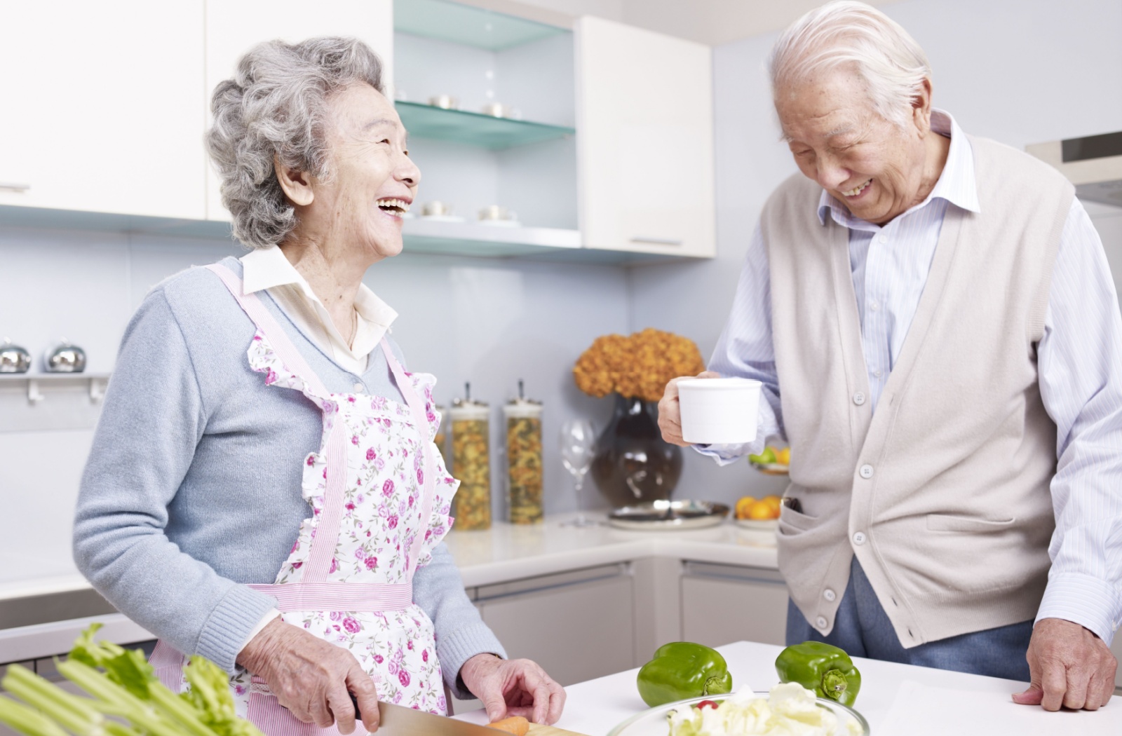 A smiling older adult man and woman preparing a bowl of salad in a kitchen