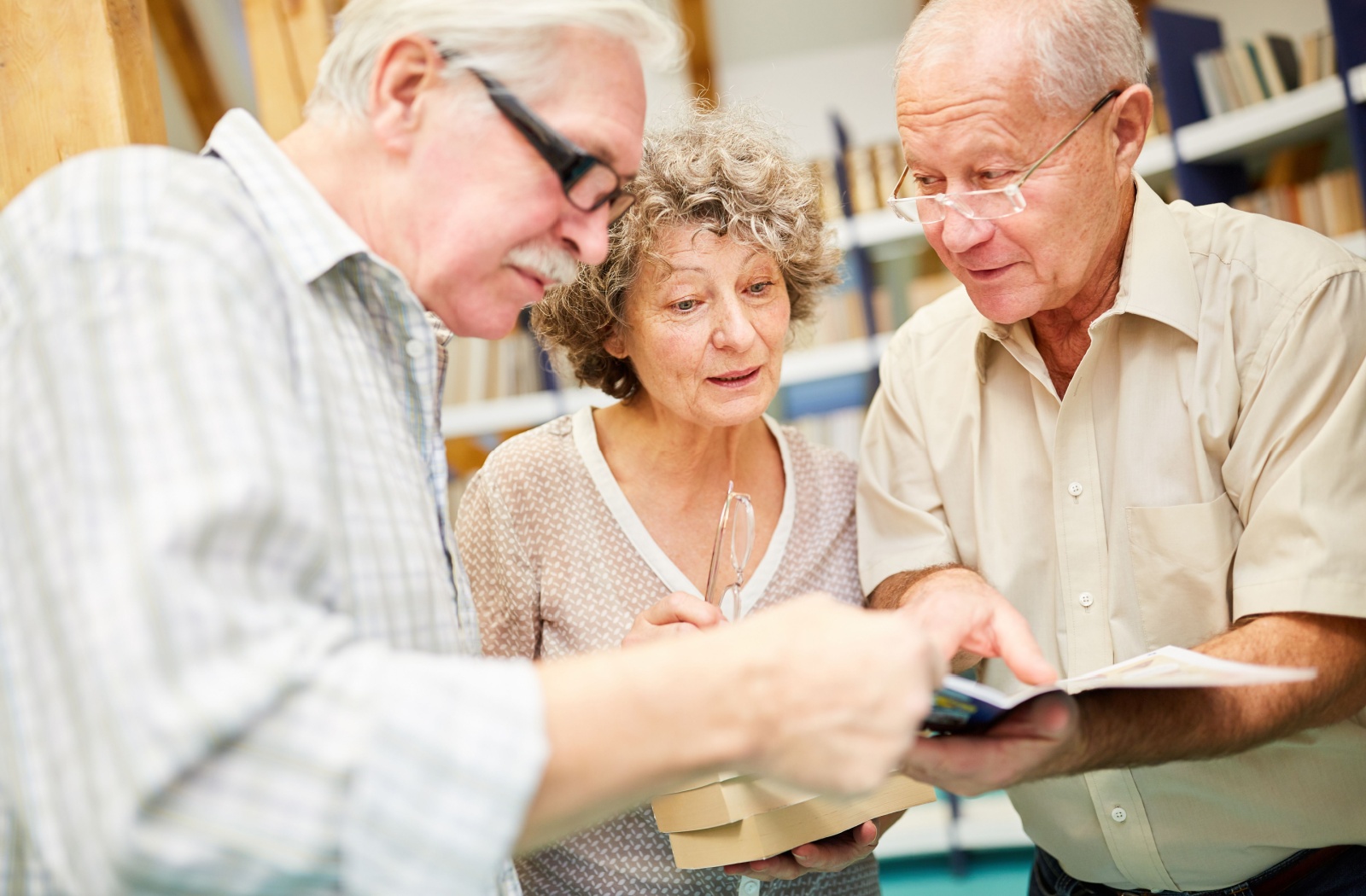 A group of older adults in a library holding and looking at a book with curiosity.