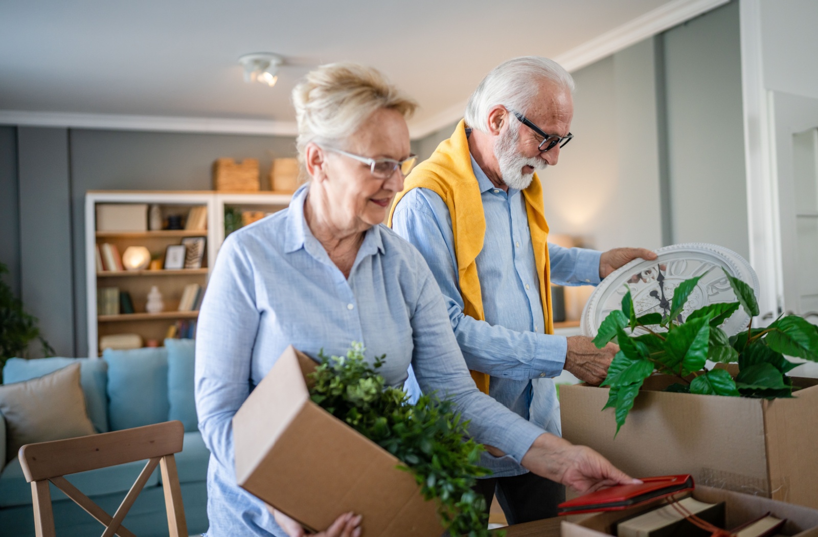 A senior couple packing belongings and plants into boxes in their home.